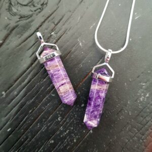 Two Charoite Double Terminated points (deep purple and pale purple facets with points at both ends), on a silver chain, on a dark wooden board