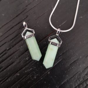 Two Chrysoprase A Grade Double Terminated points (pale green facets with points at both ends), on a silver chain, on a dark wooden board