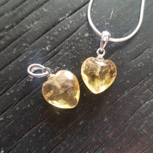 Two Citrine heart pendants - orange stone cut into a heart shape on a silver chain - on a dark wooden board