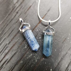 Two Kyanite A Grade Double Terminated points (pale blue facets with points at both ends), on a silver chain, on a dark wooden board