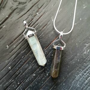 Two Labradorite Double Terminated points (grey/green facets with blue flash, points at both ends), on a silver chain, on a dark wooden board