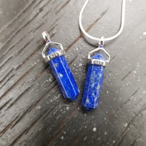 Two Lapis A- Grade Double Terminated points (dark blue with gold flecked facets, with points at both ends), on a silver chain, on a dark wooden board