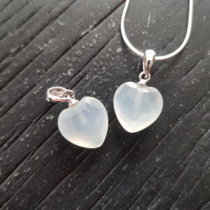 Two Moonstone heart pendants - white stone cut into a faceted shape on a silver chain - on a dark wooden board