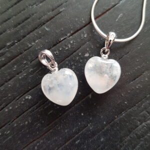 Two Rainbow Moonstone heart pendants - white stone cut into a heart shape on a silver chain - on a dark wooden board