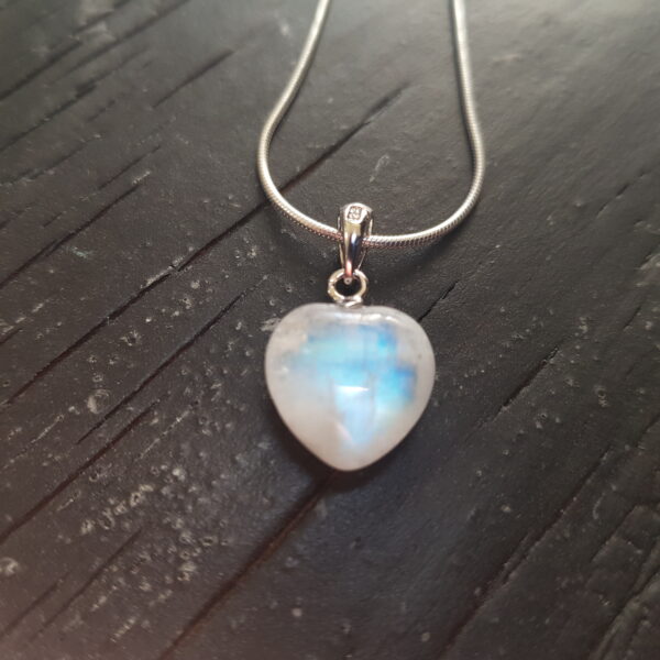 Rainbow Moonstone heart pendants - white stone cut into a heart shape on a silver chain - on a dark wooden board
