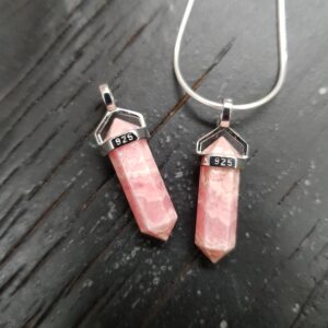 Two Rhodochrosite A Grade Double Terminated points (deep pink and pale pink banded facets with points at both ends), on a silver chain, on a dark wooden board
