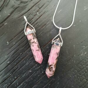 Two Rhodonite Double Terminated points (deep pink and pale pink banded facets with points at both ends), on a silver chain, on a dark wooden board