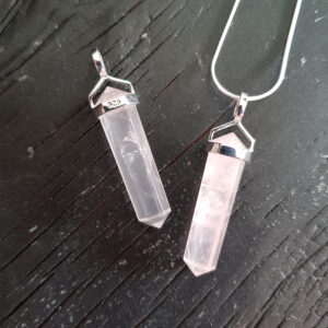 Two Rose Quartz Double Terminated points (pink facets with points at both ends), on a silver chain, on a dark wooden board