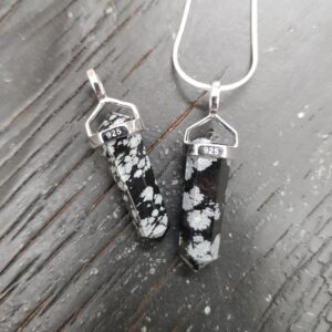 Two Snowflake Obsidian A Grade Double Terminated points (black and white patched facets with points at both ends), on a silver chain, on a dark wooden board
