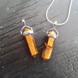 Two Tiger Eye A/A+ Grade Double Terminated points (orange and brown facets with points at both ends), on a silver chain, on a dark wooden board