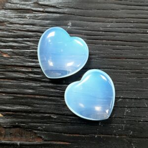 Two Opalite polished hearts, translucent blue, on a dark wooden board