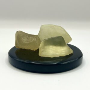 3 pieces of Libyan Desert Glass A Grade (translucent yellow stone) on a black display disk, on a white background