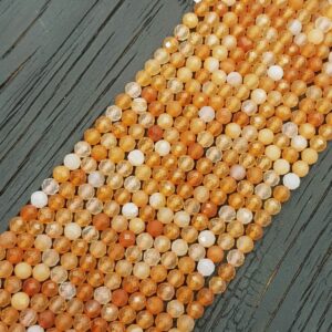 Close up of Carnelian Faceted 4mm beads - rows of small angular orange and white beads on a dark wooden board