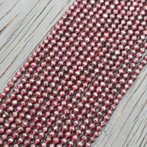 Close up of Garnet Faceted 4mm beads - rows of small angular deep red beads on a dark wooden board
