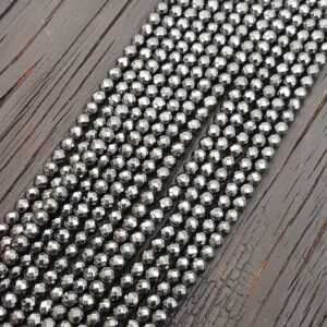 Close up of Haematin Faceted 4mm beads - rows of small angular metallic beads on a dark wooden board