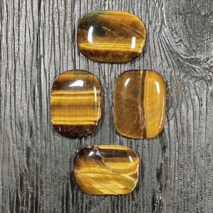 Four Tiger Eye Rectangle Stones, gold and brown banding, on a black wooden board