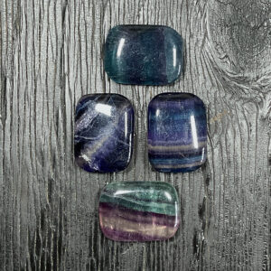 Four fluorite rectangle stones, green, purple, blue banded, on a black wooden board