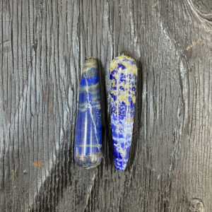 Two Lapis Lazuli Wands, blue with white and gold banding, on a black wooden board.