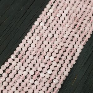 Close up of Rose Quartz Faceted 4mm beads - rows of small angular pale pink beads on a dark wooden board