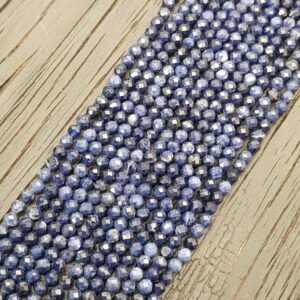 Close up of Sodalite Faceted 4mm beads - rows of small angular blue with white and grey beads on a dark wooden board