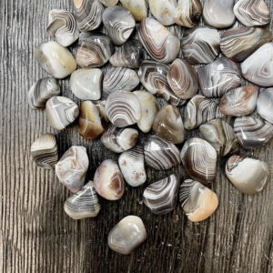 Example of Grey Agate tumble stones - grey stones with white and black banding - on a dark wooden board