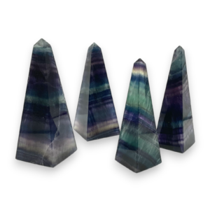 Four obelisks in a row - purple, green and see through banded fluorite - on a white background