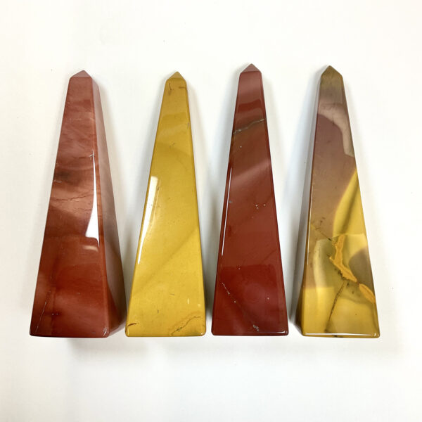 Four obelisks in a row - alternating red and yellow Mookaite - on a white background