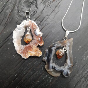 Two Geode Slice with Citrine Pendants - cream or grey circular agate, with a natural orange Citrine (heat treated) point suspended inside - on a dark wooden board