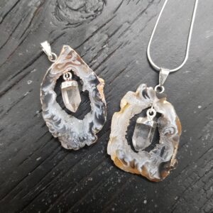 Two Geode Slice with Quartz Pendants - cream or grey circular agate, with a natural clear quartz point suspended inside - on a dark wooden board