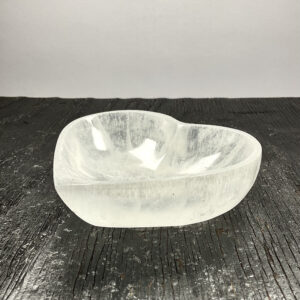 One Selenite Heart Bowl from the side - translucent white stone - on a black wooden board