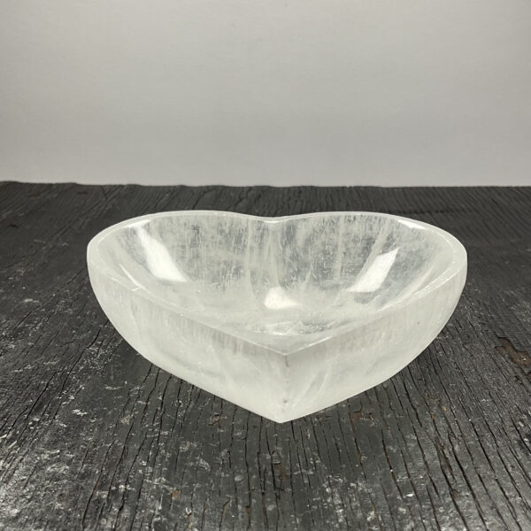 One Selenite Heart Bowl from the front - translucent white stone - on a black wooden board