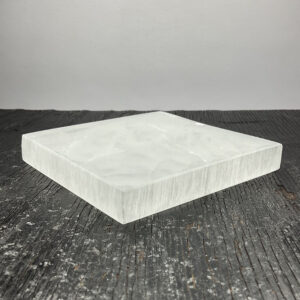 One Charging Plate (Square) - Selenite from the side - translucent white stone carved into the shape of a square - on a dark wooden board