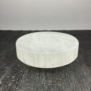 One Charging Plate (Circle) - Selenite from the side - translucent white stone carved into the shape of a circle - on a dark wooden board