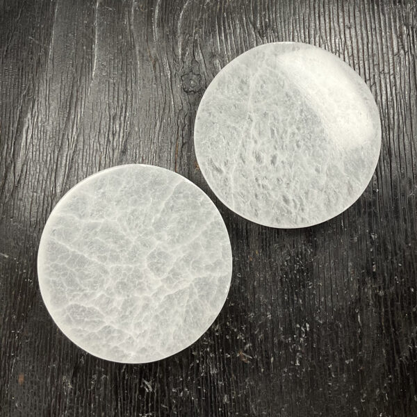Two Charging Plate (Circle) Selenite from above - translucent white stone carved into the shape of a circle - on a dark wooden board