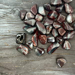Example of Ancestralite tumble stone - black stone with dark red and sparkly grey banding - on a black background