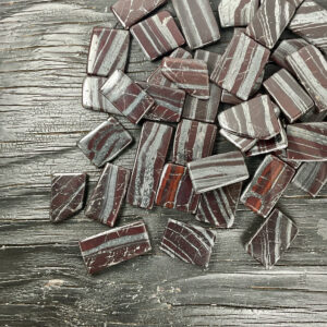 Example of Ancestralite Slices tumble stone - black stone with dark red and sparkly grey banding - on a black background