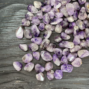 Example of Amethyst Brandberg tumble stone - translucent stones of purple, clear and grey - on a black, wooden background