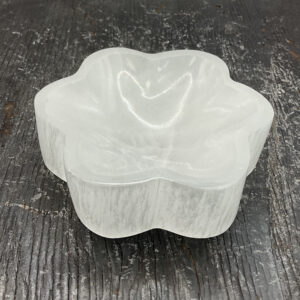 One Selenite Flower Bowl from the side - translucent white stone carved into the shape of a flower - on a black wooden board