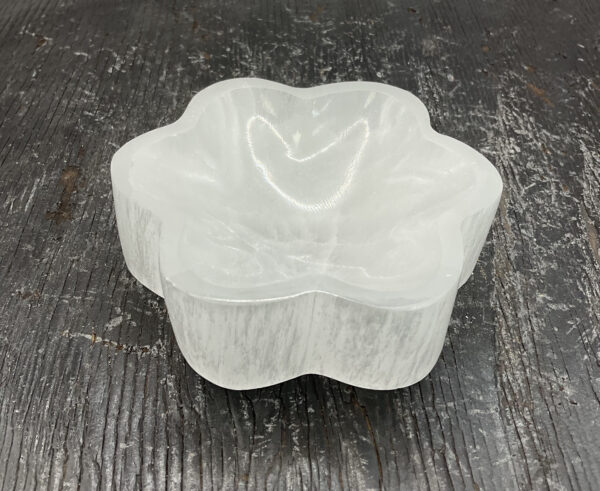 One Selenite Flower Bowl from the side - translucent white stone carved into the shape of a flower - on a black wooden board