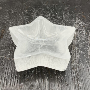 One Selenite Star Bowl from the side - translucent white stone carved into the shape of a star - on a black wooden board