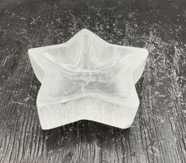 One Selenite Star Bowl from the side - translucent white stone carved into the shape of a star - on a black wooden board