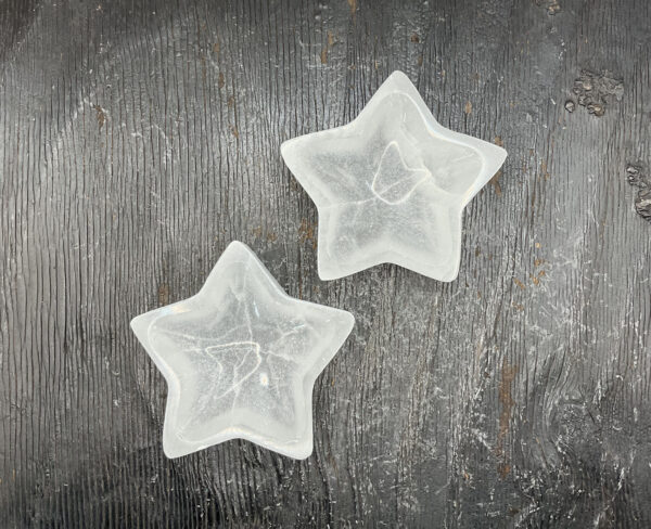 Two Selenite Star Bowls from the side - translucent white stone carved into the shape of a star - on a black wooden board